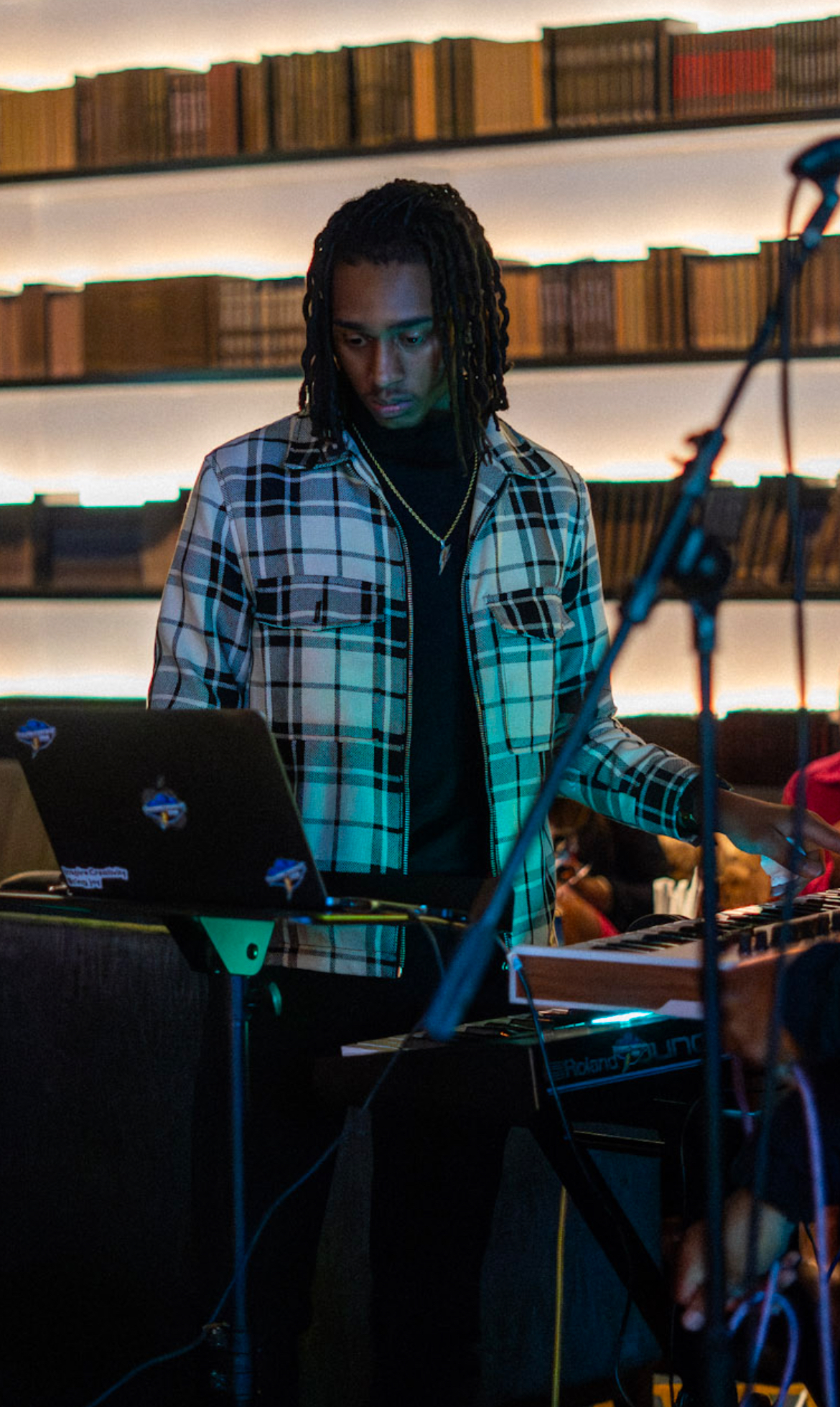 Caleb Lewsey playing a Roland keyboard under teal stage light during a live set